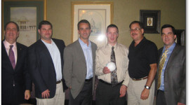 Lion Secretary Dave Tanner, Tailtwister Tom Jacoberger, President Chris Lopez, and Treasurer Mike Schwargel are shown in the attached photo presenting the Club’s $1000 donation to representatives of the LI Bombers.